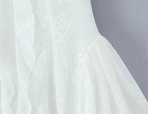 Detail of white lace fabric featuring floral embroidery and mesh texture on the dress