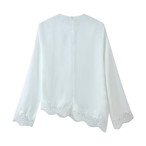 Detail of white long sleeve top featuring intricate lace trim and wavy asymmetrical hem