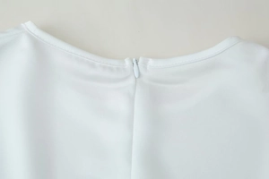 Close-up of the round neckline and invisible zipper on the white lace patchwork top
