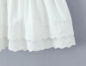 Detailed close-up of double-layered white eyelet embroidery on a pleated dress hem