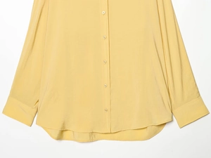 Détail d'une chemise jaune pâle à manches longues, texture soie et boutons simples
