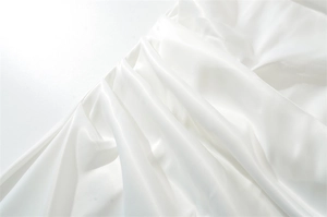 Close-up of white satin fabric with soft pearlescent luster and elegant gathered pleats