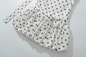 Detail of white dress with black polka dots featuring a waist bow and ruffled hem