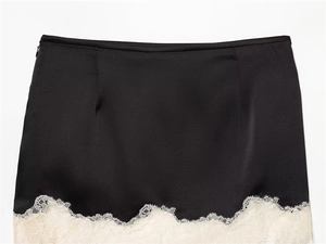 Détail de mini-jupe en satin noir avec dentelle de cils blanche et fermeture éclair latérale
