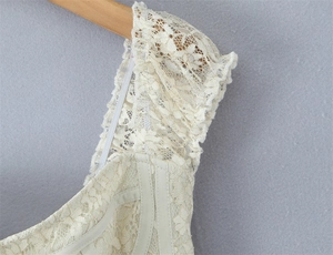Detail of cream lace dress shoulder showing floral patterns and elastic straps on wood hanger
