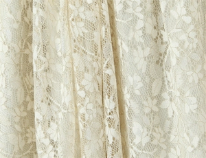 Close-up of cream floral lace fabric with intricate crochet patterns and mesh texture