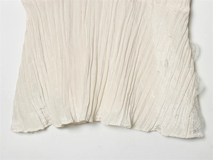 Detailaufnahme von weißem Plissee-Stoff mit eleganter Spitze und romantischer Textur