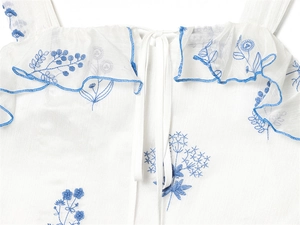 Detail of blue floral embroidery and ruffle trim on a white off-shoulder dress