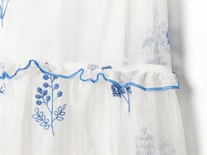 Close-up of white dress with blue plant embroidery and layered ruffle edge detail