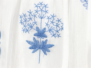 Macro shot of blue floral embroidery on white ruffle off-shoulder dress fabric