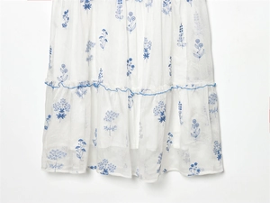 Detailed view of white floral dress with navy embroidery and ruffled layered hemline
