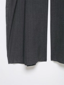 Détail du pantalon à rayures gris foncé montrant le tissu drapé et l'ourlet tailleur