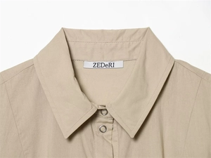 Detail of khaki shirt collar with silver metal snap buttons and stitched brand label