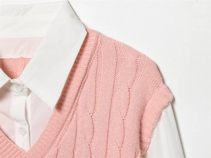 Détail de l'épaule d'un gilet en tricot rose avec broderie sur une chemise blanche