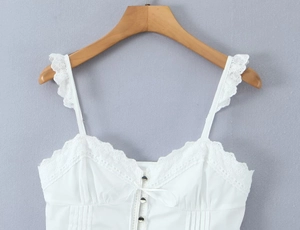 Detail of white cotton camisole featuring lace embroidery, pintuck pleats and buttons