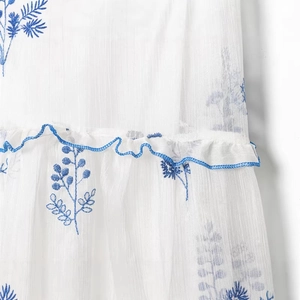 White off-shoulder dress featuring blue floral embroidery and elegant ruffle edge details
