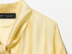 Detailed macro view of pale yellow satin shirt collar with elegant decorative tie design
