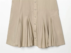 Detail of khaki pleated dress featuring metallic snap buttons and fabric texture