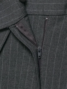 Détail de la braguette à glissière et des rayures verticales sur le pantalon gris
