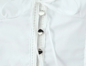 Detail of white lace trim, silver metal buttons and satin ribbon tie on women's top
