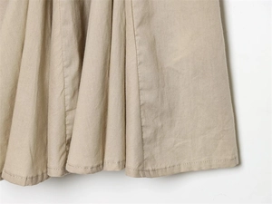 Macro detail of beige woven cotton fabric showing hem stitching and texture on the dress
