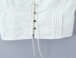 Close-up of white top featuring silver heart buttons, lace trim and pleated details