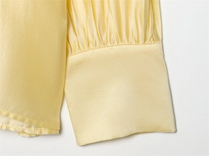 Detail of pale yellow satin long sleeve cuff with subtle pleats and fine stitching