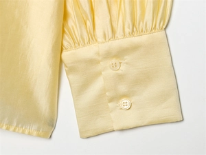 Close-up of light yellow silk blouse cuffs featuring fine pleats and dual button details