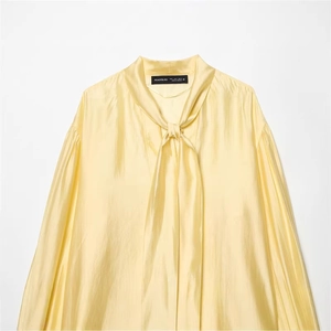 Detailed view of yellow satin shirt featuring pussy-bow tie neck and silky fabric texture