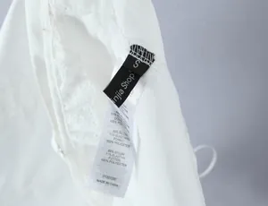 Detail shot of the care label and size tag on white lace camisole top for women