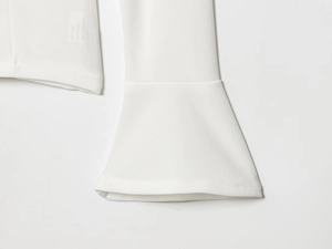 Dettaglio del top bianco con scollo a V che mostra il polsino a campana e la trama del tessuto