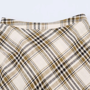Detail view of the asymmetric plaid skirt waist showing green and cream fabric texture