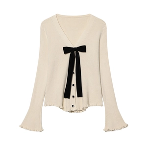 Dettaglio del cardigan in maglia crema con bottoni a cuore neri e grande fiocco di velluto