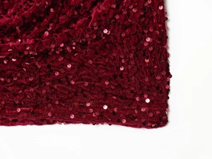 Détail macro du tissu à paillettes rouge vin sur une robe moulante en velours