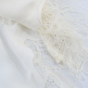Close-up of fine white lace fabric with delicate eyelash trim on a satin garment edge