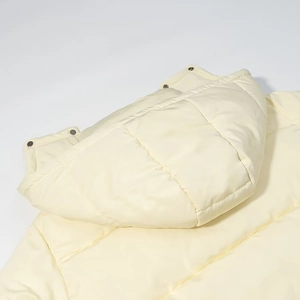 Detail view of the quilted cream yellow hooded winter puffer coat with metal snap buttons