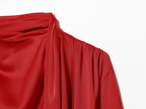 Detailed view of women's red satin blouse featuring a draped neckline and shoulder pleats