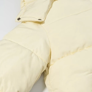 Detail of cream winter puffer jacket featuring quilted texture and metallic snap buttons