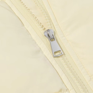 Macro shot of silver metal zipper slider and teeth on a light yellow winter jacket