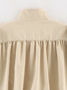 Detail view of the gathered pleats and stand collar on the back of a beige jacket