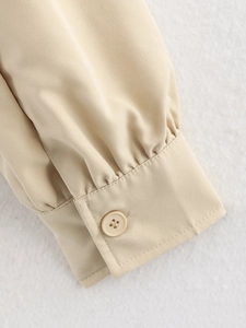 Close-up of pleated cuffs and single button on a light beige cropped jacket sleeve