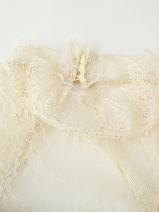 Détail macro du décolleté en dentelle blanc crème avec texture mesh et bouton de fermeture