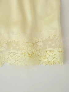 Détail d'un haut en satin crème avec bordure en dentelle florale et broderie raffinée