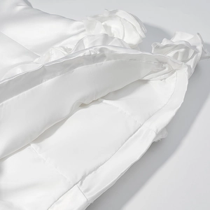 Detail of white satin dress featuring elegant tiered ruffles and smooth silk texture