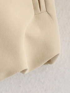 Detailed macro view showing beige textured fabric and fine stitching on a cropped jacket