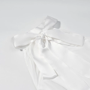 Detailed view of the white satin halter neck dress featuring a large elegant bow tie