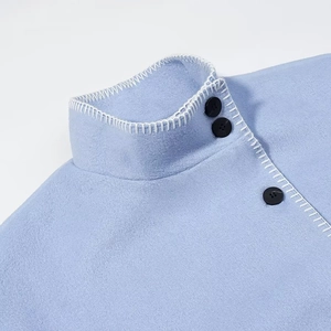 Detailed close-up of light blue wool coat with white contrast stitching and black buttons