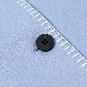 Detail of blue wool fabric featuring a black button and decorative white stitching work