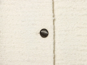 Macro shot of striped gold metal button on luxury cream-white tweed jacket fabric