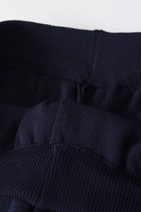 Detailed close-up of navy knit trousers showing elastic waistband and ribbed texture